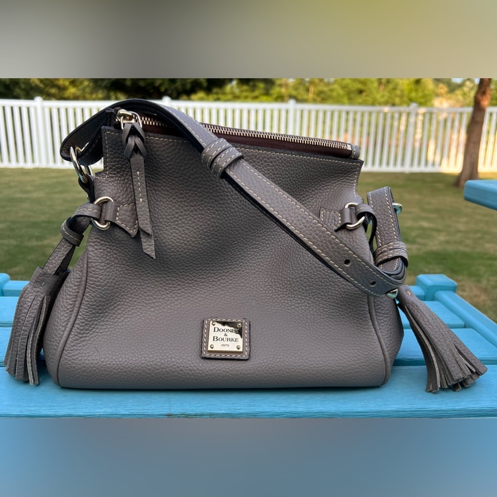 Dooney & Bourke pebbled leather tassel shoulder bag. Color is a grayish/tan.